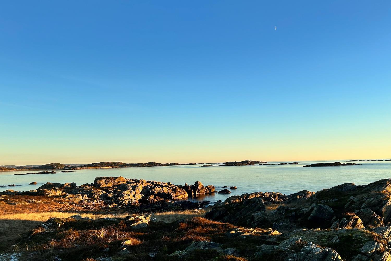 Steinete kystlandskap i lav sol ved rolig sjø.